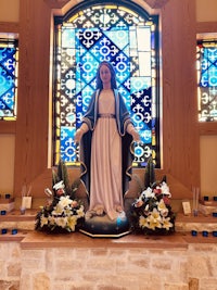 a statue of mary in front of a stained glass window